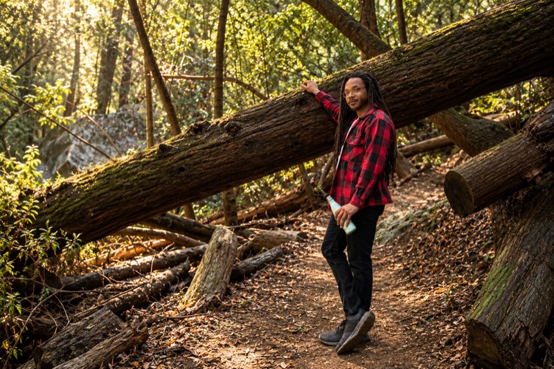 D'Marcus Butler leaning against a fallen tree on a forest trail